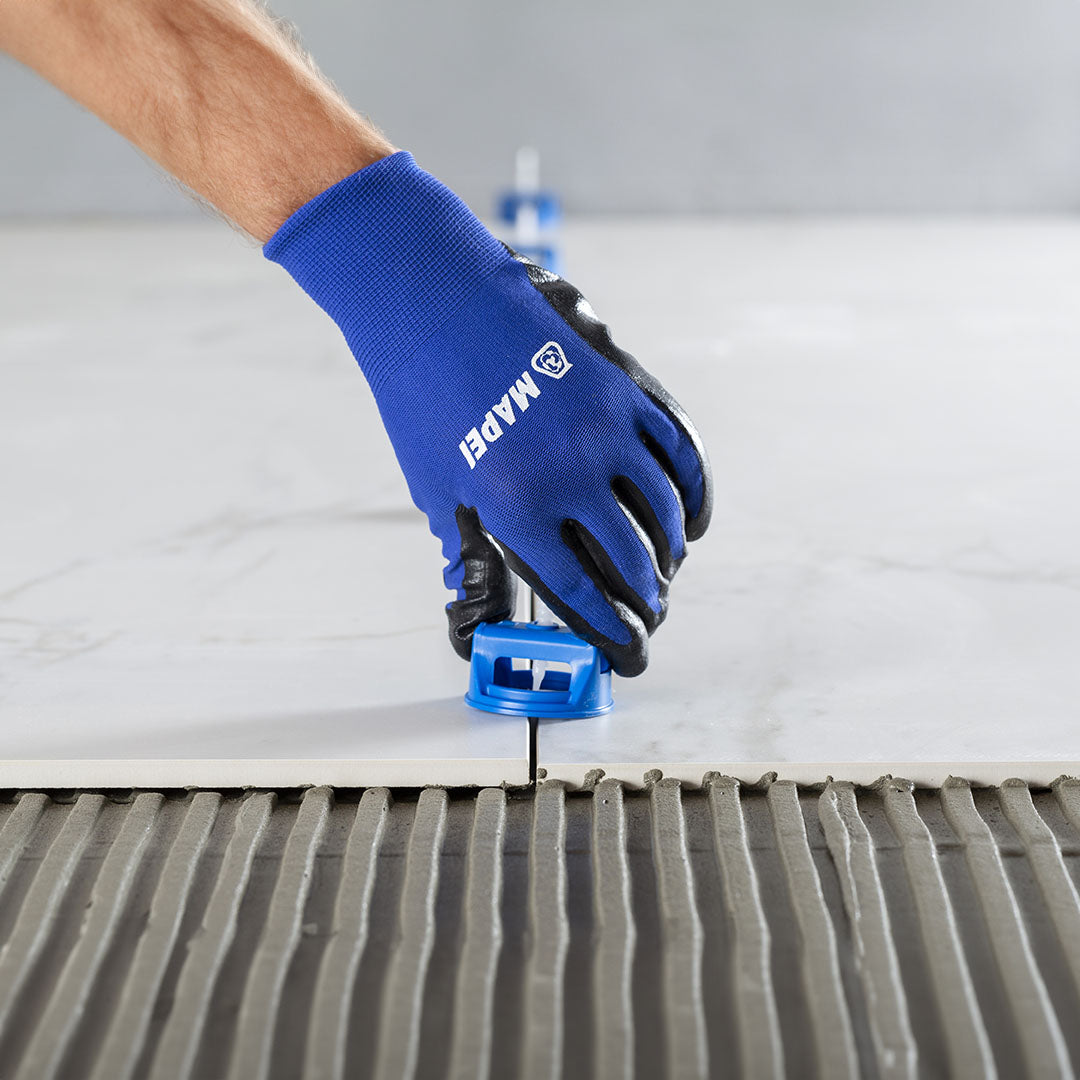 A hand wearing gloves uses the Mapei MapeLevel Easyclick Cap to level ceramic tile during installation.