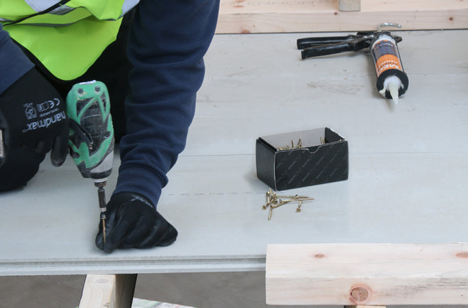 Worker using a drill to install STS TG4 Cement Board 22mm on construction site.